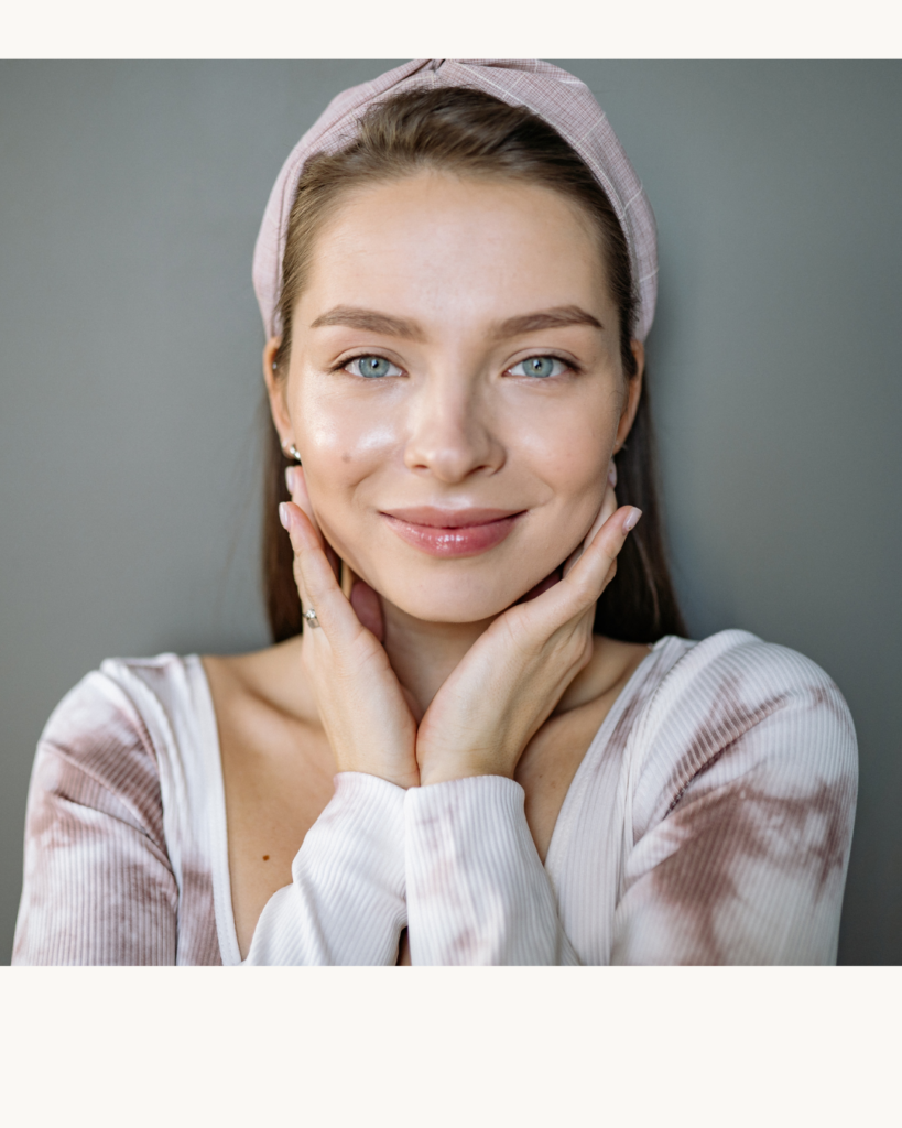 “Woman with a soft, natural expression gently touching her face, wearing a headband and neutral clothing against a plain background