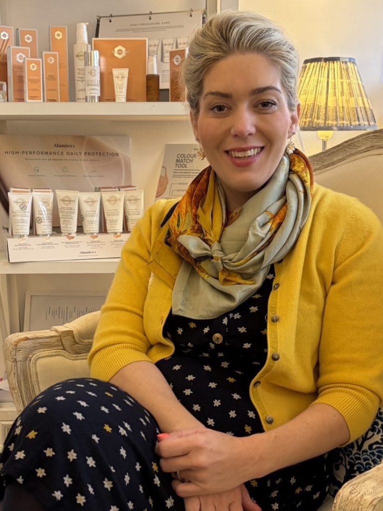 Dr Halliday seated in the Blue Bird Aesthetics consulting room with skincare displays behind her.