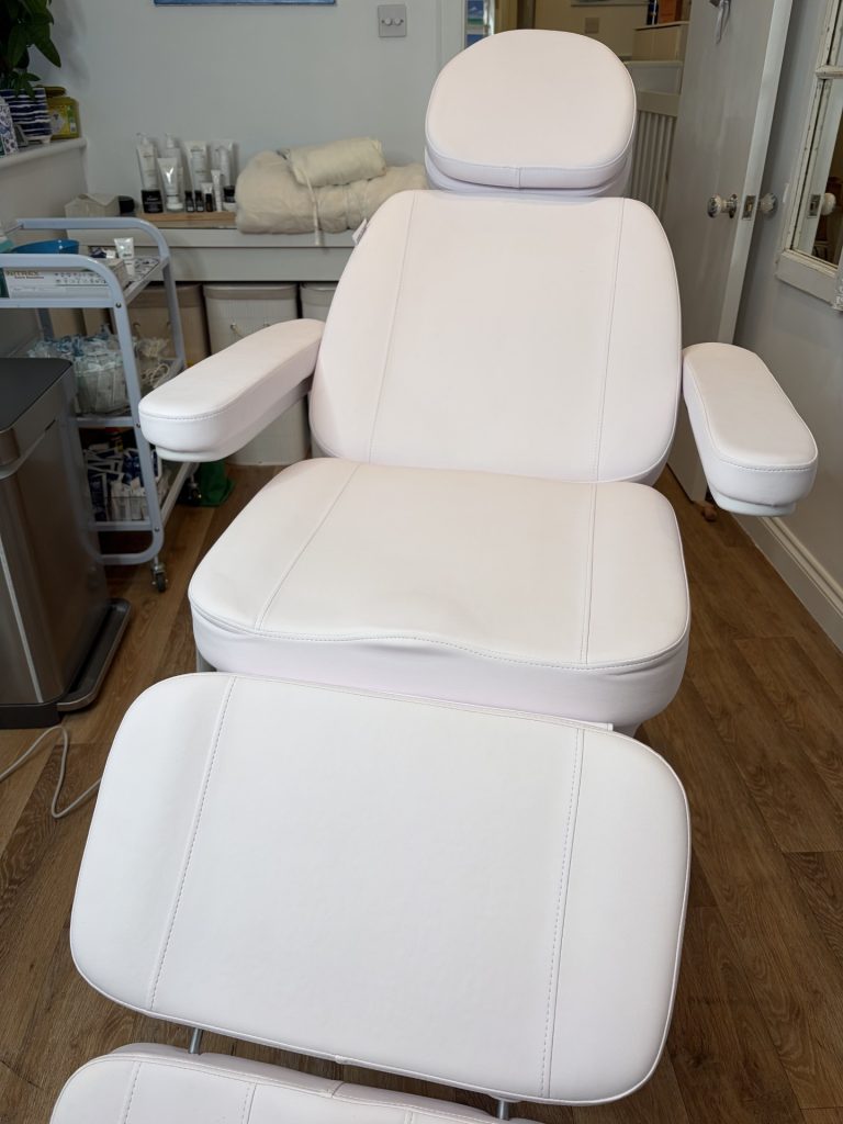 Clean aesthetic treatment room with white reclining heated chair and organised equipment.